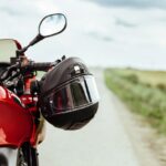 Schwarzer Motorradhelm am Lenker eines roten Motorrads mit Blick auf eine Landstraße – wichtiges Motorrad Zubehör für Sicherheit & Komfort.