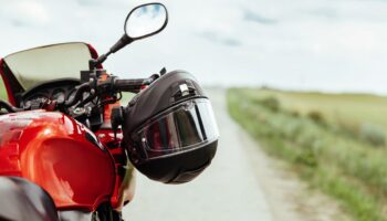 Schwarzer Motorradhelm am Lenker eines roten Motorrads mit Blick auf eine Landstraße – wichtiges Motorrad Zubehör für Sicherheit & Komfort.