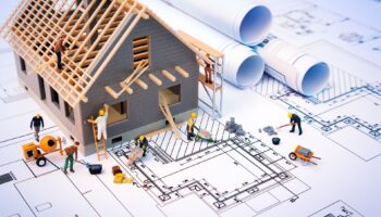 Modellhaus auf Bauplan mit Miniaturfiguren