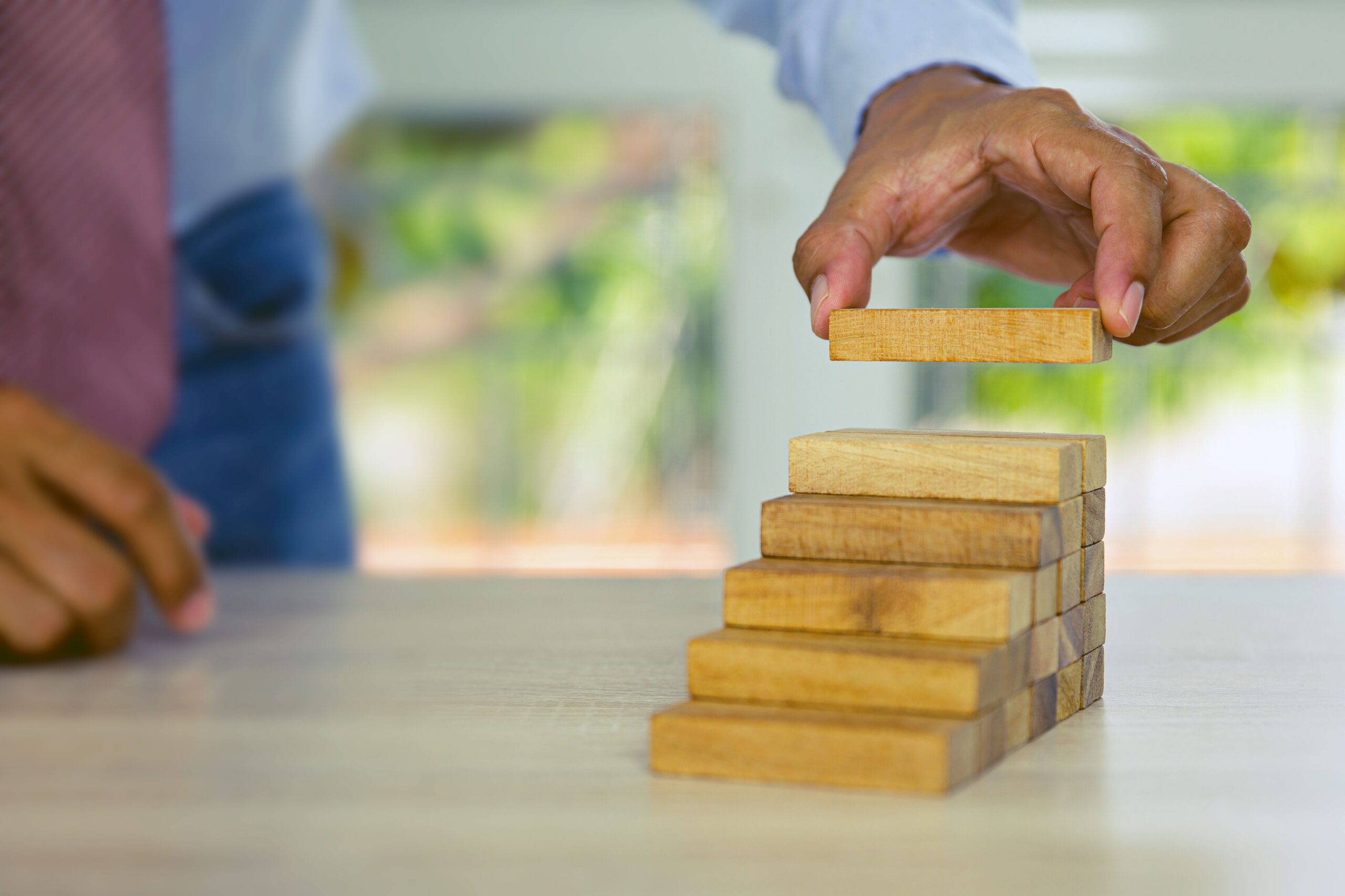 Hand platziert ein Holzbauteil auf einer kleinen Modelltreppe, um beim Treppen planen strukturiert Abläufe zu visualisieren