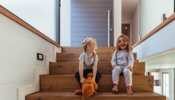 Lachende Kinder auf breiten Holzstufen zeigen, wie wichtig Sicherheit beim Treppen planen sind